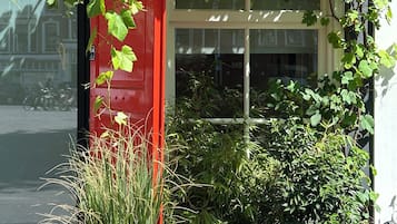 Een rode structuur met klimplanten en begroeiing, een raam en een gevel.