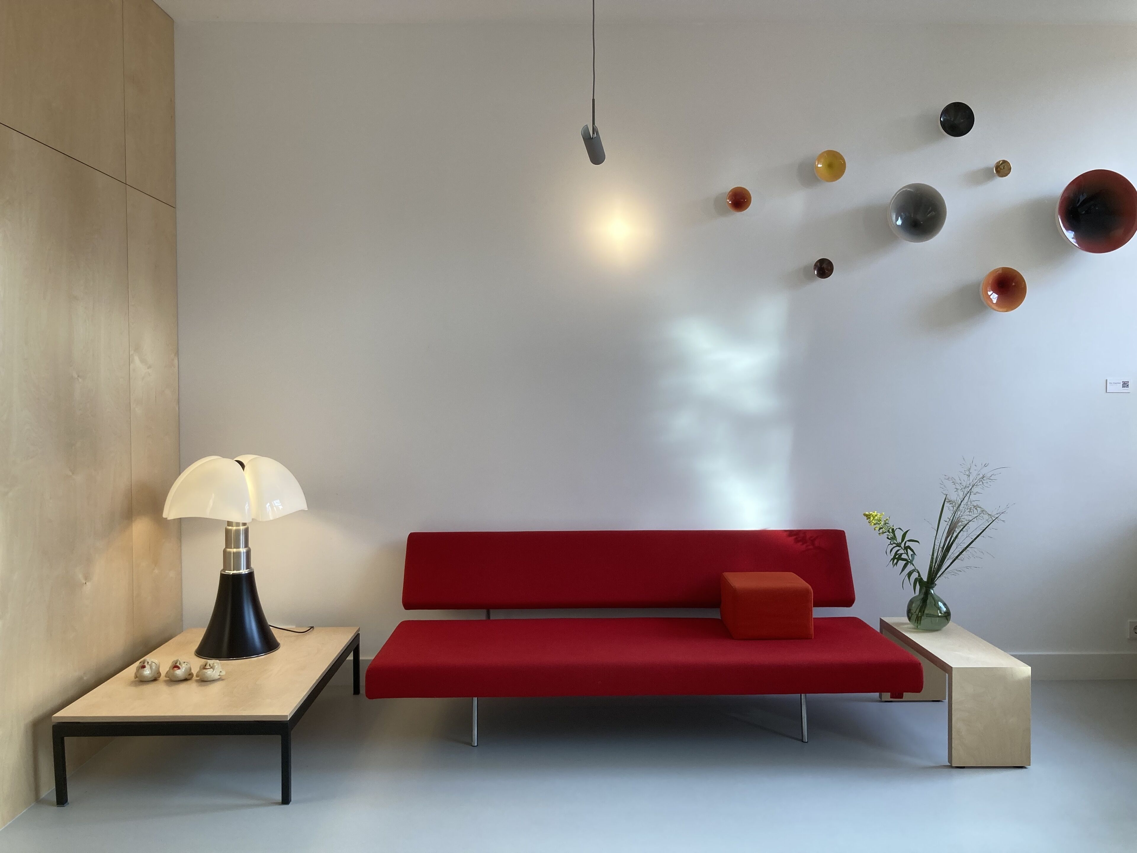 A modern living room with a red sofa, a small table with a lamp, and a wall decorated with spherical objects.