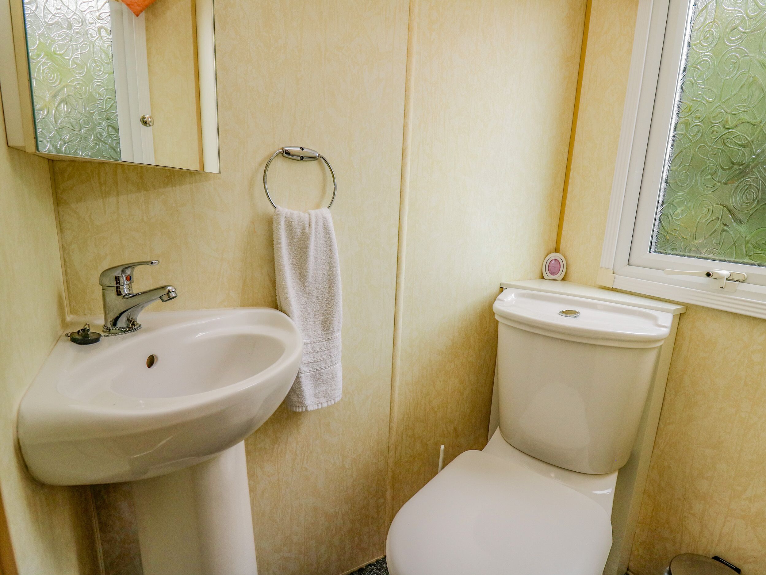 Et badeværelse med en hvid vask, toilet og et vindue med udsigt til grønne omgivelser.