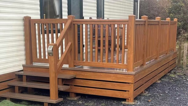 Een stacaravan met een houten terras en een trap die naar de ingang leidt.