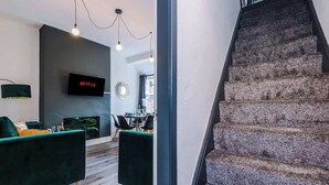 Ein modernes Wohnzimmer mit Flachbildfernseher, grünen Sofas und einem Essbereich mit rundem Spiegel.