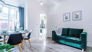 Ein modernes Wohnzimmer mit einem grünen Sofa, einem Esstisch mit Stühlen und einem großen Fenster mit Vorhängen.
