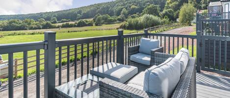 A balcony with wicker furniture, a view of a green landscape, and a distant communication tower.