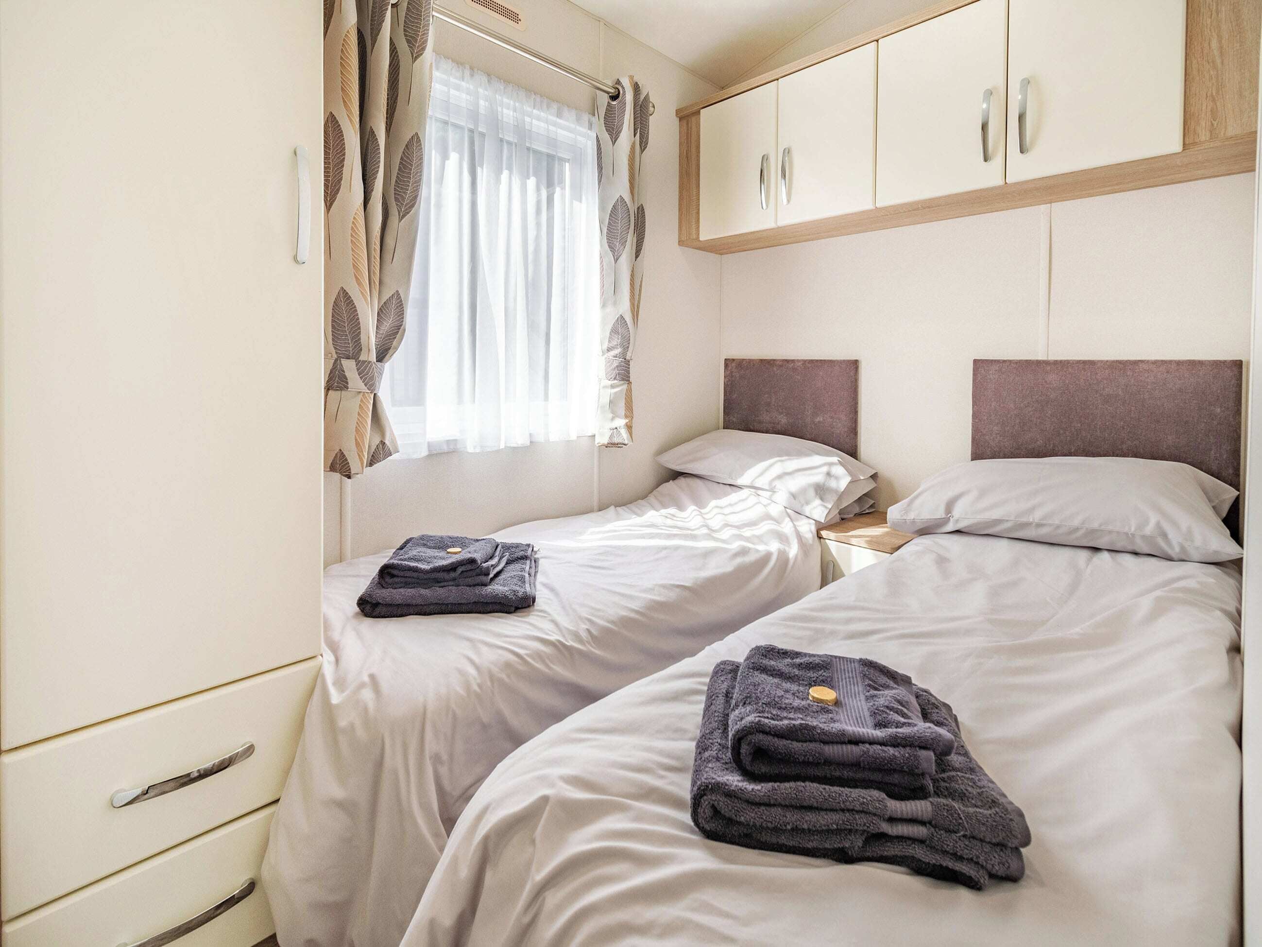 A bedroom with two beds, a window with curtains, and a wardrobe.