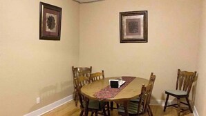 Ein Esszimmer mit Holztisch und Stühlen, einem gemusterten Teppich und zwei gerahmten Bildern an den Wänden.