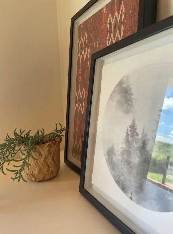 A framed artwork with a landscape scene, a woven basket with greenery, and a patterned wall hanging. - MooseHaven Lake house. Hot tub + Stunning views (Ashmont)