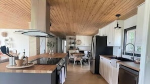 A modern kitchen with a wooden ceiling, a central island, and a dining area in the background.