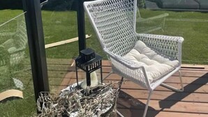 A white wicker chair on a wooden deck with a view of a lake and hills.