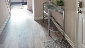 Un couloir avec une console en verre, des plantes en pot et une porte dotée d’une poignée en laiton.