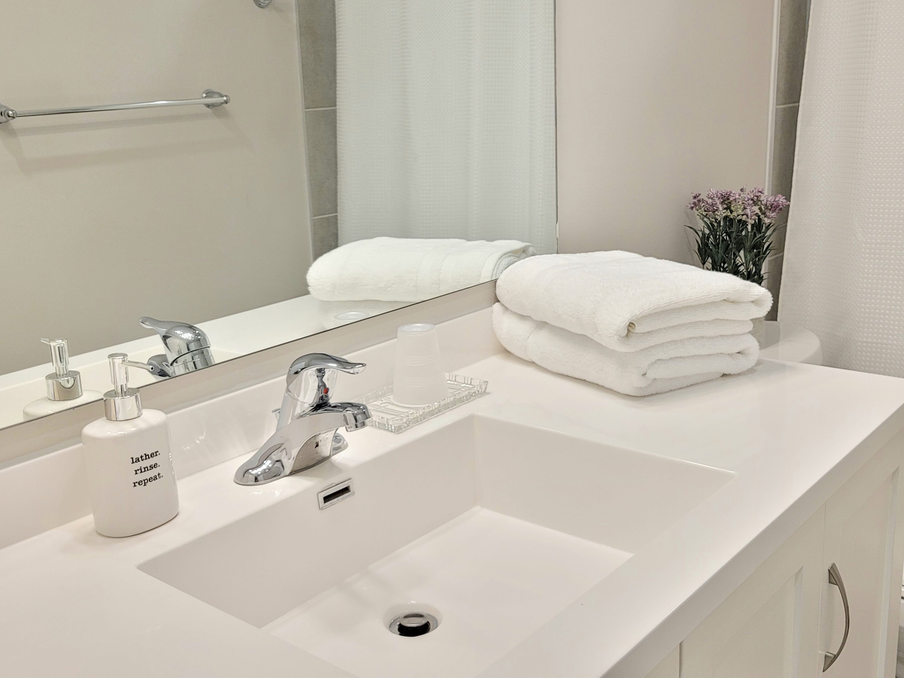 A modern bathroom with a white sink, a mirror, and a towel rack.