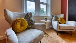 Two grey armchairs with patterned cushions, a small white table with a plant, and a window with a view of trees. - Haworth Heights (Keighley)