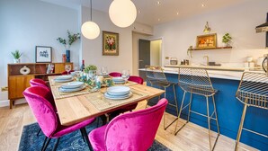 A modern kitchen with a wooden island, bar stools, and a dining area with a wooden table and pink chairs. - Haworth Heights (Keighley)