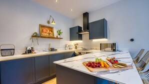 A modern kitchen with dark cabinets, a marble countertop, and a central island with a fruit display. - Haworth Heights (Keighley)