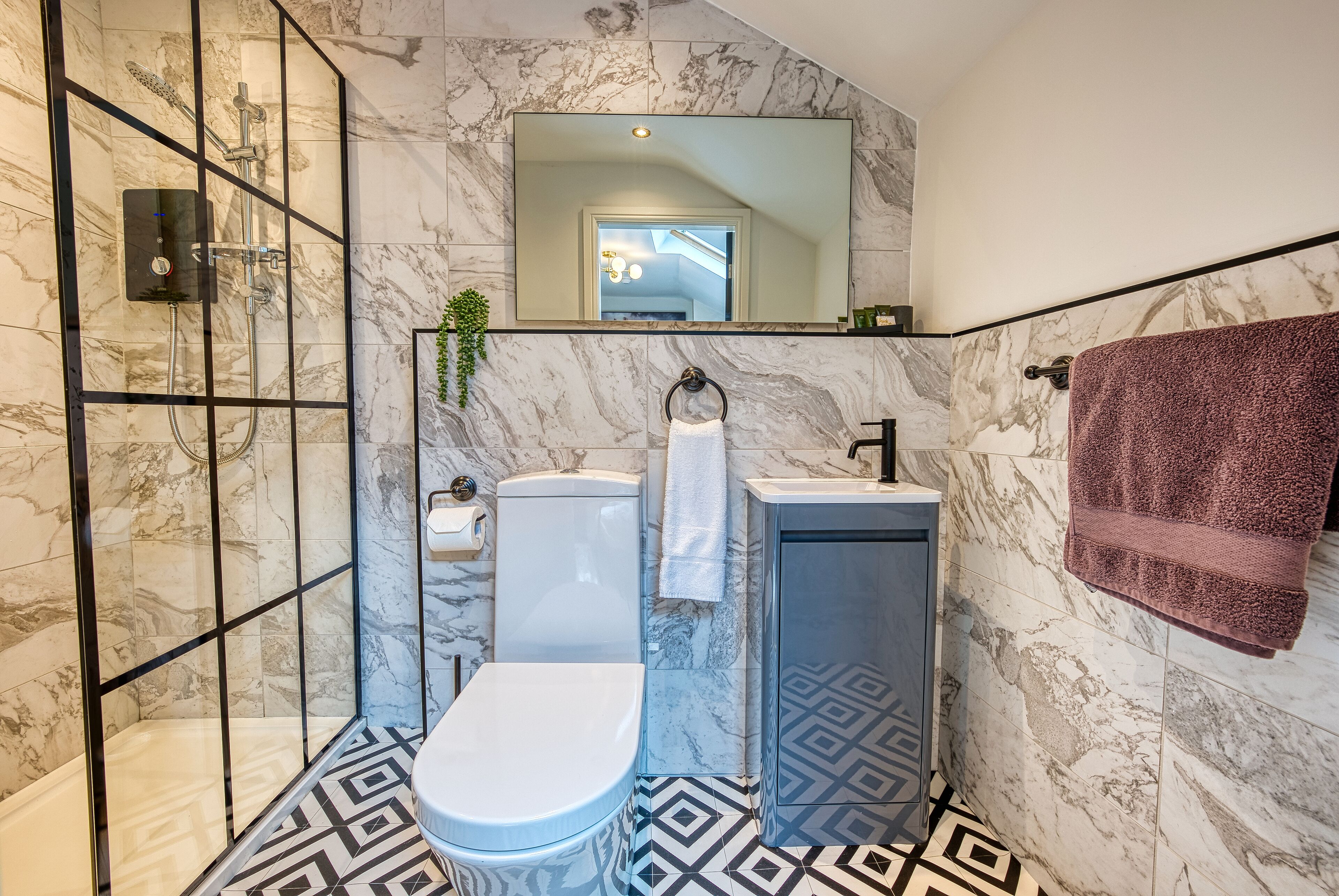 A bathroom with a shower, toilet, and sink, all with marble walls and a geometric patterned floor.
