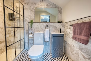 A bathroom with a shower, toilet, and sink, all with marble walls and a geometric patterned floor.