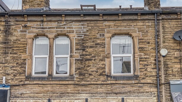 A stone building with a dark blue door, multiple windows, and a small garden area. - Haworth Heights (Keighley)