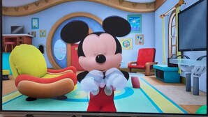 A television displaying a cartoon character in a room with a large window, a red chair, and a yellow chair. - Apartment Luxe Next to Malls Central Location (Georgetown)