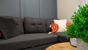 Uma sala de estar moderna com um sofá modular cinza escuro, uma mesa de centro redonda de madeira e um vaso com planta.