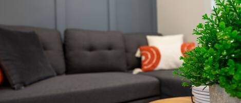 Een moderne woonkamer met een donkergrijze modulaire bank, een ronde houten salontafel en een potplant.