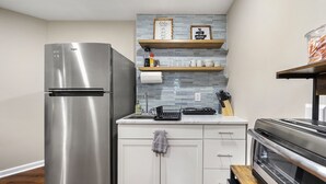 Uma cozinha com geladeira de aço inoxidável, forno embutido, prateleiras de madeira e painel de azulejos.