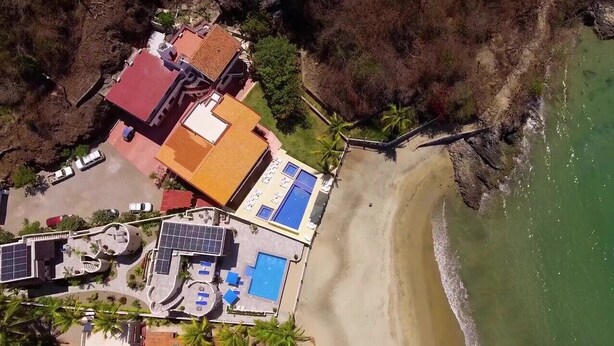 Vista aérea de una propiedad costera con piscina, paneles solares y una playa.