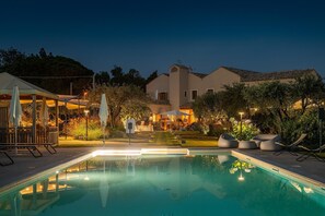 A swimming pool with a deck, surrounded by outdoor seating and a building in the background. - Locanda Della Meridiana - Cappero (Pula)