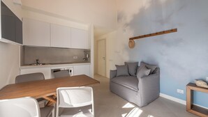 A compact living space with a kitchenette, a dining area, and a seating area with a sofa and chairs. - Locanda Della Meridiana - Cappero (Pula)