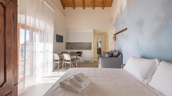 A modern bedroom with a large bed, a desk, and a kitchenette. - Locanda Della Meridiana - Cappero (Pula)