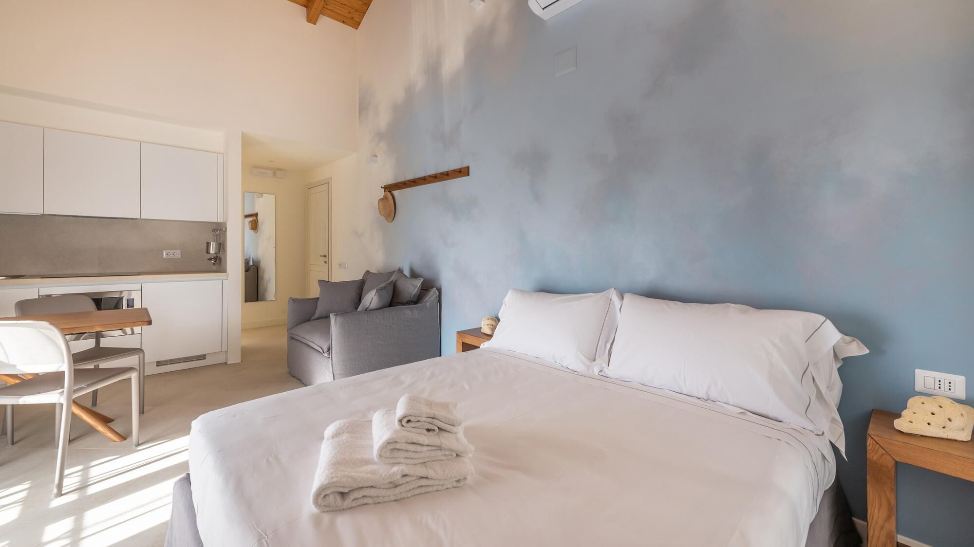Una camera da letto con un letto, un comodino, una sedia, un divano e una piccola cucina sullo sfondo.