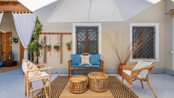 A cozy outdoor seating area with a wooden bench, two wicker chairs, and a blue sofa. There are two decorative wooden tables and a patterned rug on the floor. - Locanda Della Meridiana - Olivo (Pula)