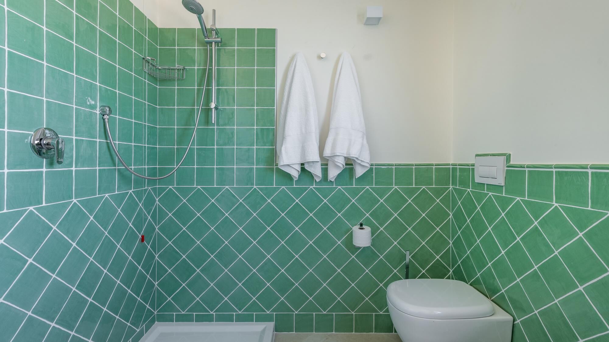A bathroom with green tiled walls, a white toilet, and a shower.