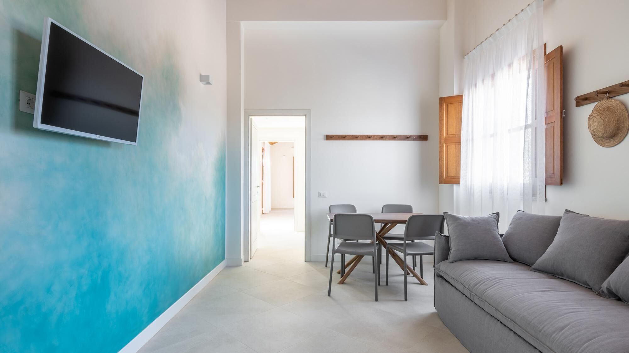 A modern living room with a grey sofa, a dining table with chairs, and a TV mounted on the wall.