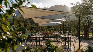 An outdoor dining area with tables and chairs under a canopy, surrounded by trees and a mountainous backdrop. - Locanda Della Meridiana - Ginepro (Pula)