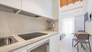 A modern kitchen with a built-in stove, a sink, and a dining area with a table and chairs. - Locanda Della Meridiana - Ginepro (Pula)