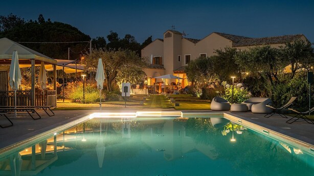 A swimming pool with a deck, surrounded by outdoor seating and a building in the background. - Locanda Della Meridiana - Ginepro (Pula)