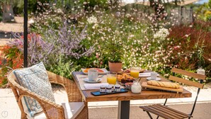 An outdoor dining table with breakfast items, a wicker chair, and a garden in the background. - Locanda Della Meridiana - Oleandro (Pula)