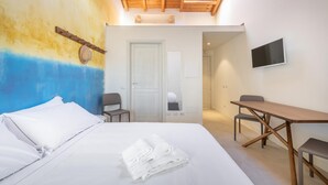 A bedroom with a bed, a desk, a chair, a TV, and a door leading to another room. - Locanda Della Meridiana - Oleandro (Pula)