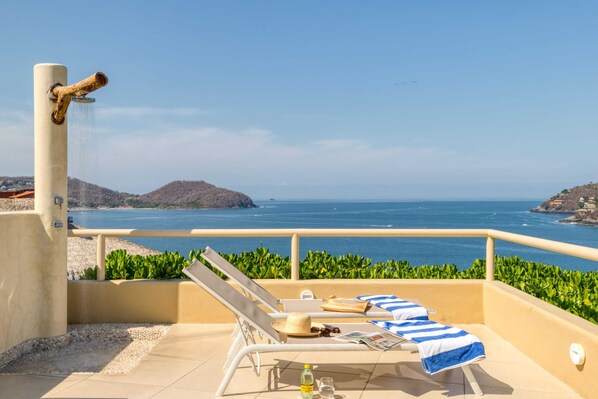 A balcony with two sun loungers, a water feature, and a view of the sea.