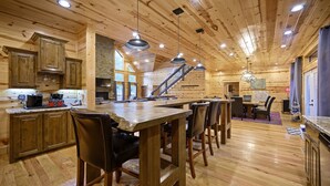 Une cuisine spacieuse avec des meubles en bois, un grand îlot central doté de tabourets et une cheminée en pierre.