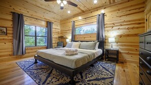 Une chambre à coucher située dans une cabane en bois, comprenant un lit, deux fenêtres, un ventilateur de plafond et une table de chevet.