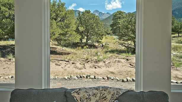 Ein Zimmer mit großem Fenster und Blick auf eine bewaldete Berglandschaft unter blauem Himmel.