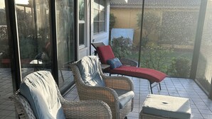 En overdækket terrasse med fletningsmøbler, heriblandt en sofa og to skodder, samt en rød liggestol.