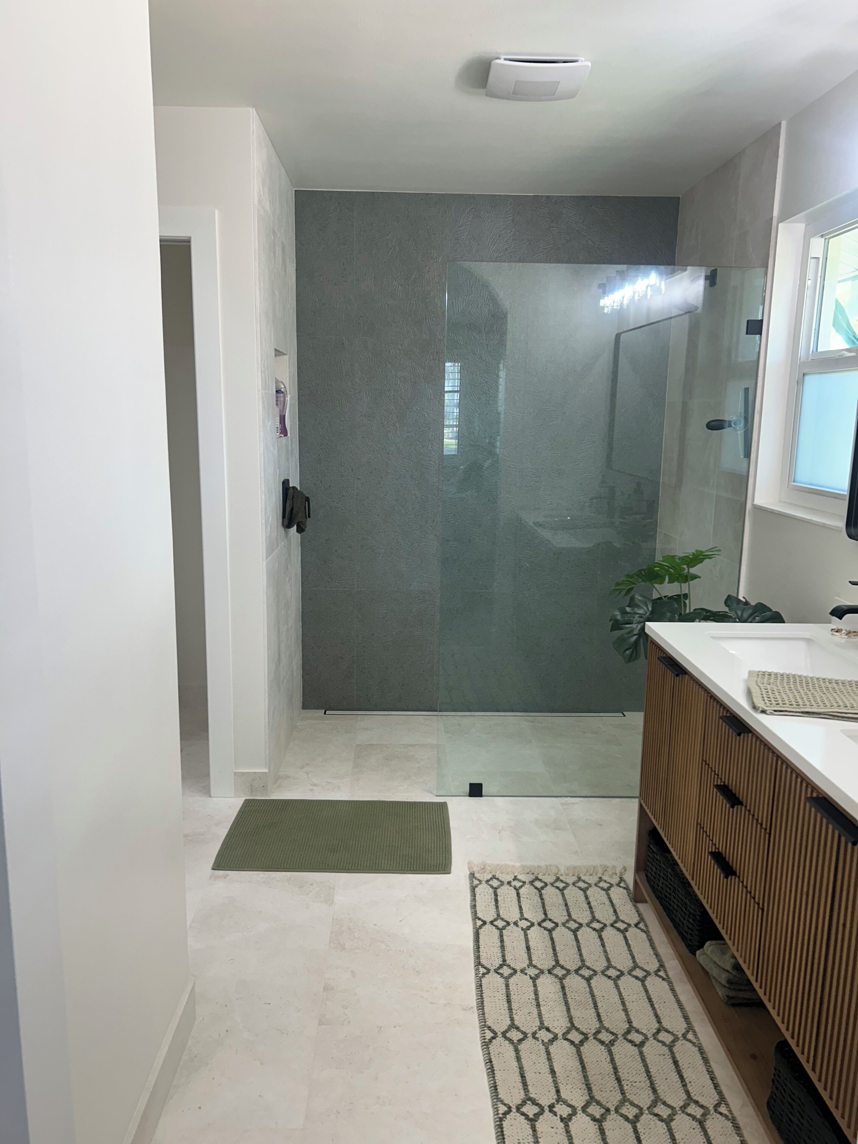Une salle de bain moderne avec une porte de douche en verre, un lavabo blanc et un meuble-lavabo en bois.