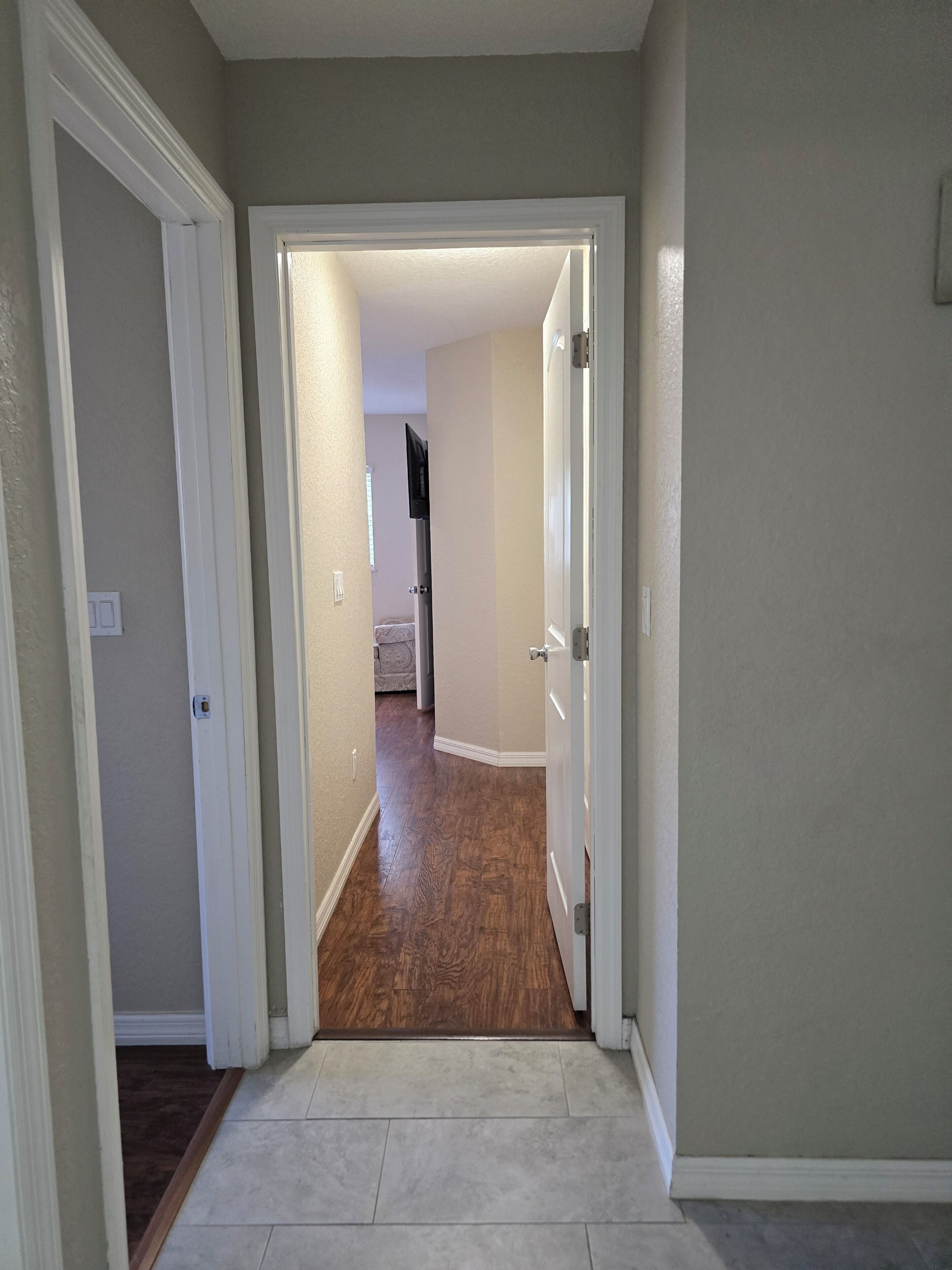 A hallway with a wooden floor, white walls, and a door leading to another room.