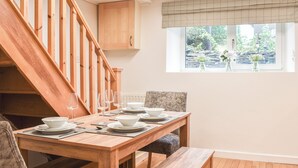 Un comedor con una mesa de madera dispuesta para cuatro personas, un banco y una escalera con barandillas de madera que conduce a un espacio superior.