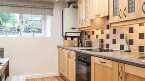 Una cocina con armarios de madera, horno integrado, cafetera y ventana con vista a follaje.
