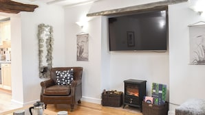 Una sala de estar con un sillón de cuero marrón, una mesa de centro de vidrio con objetos decorativos, una chimenea con leña y un televisor de pantalla plana montado en la pared.