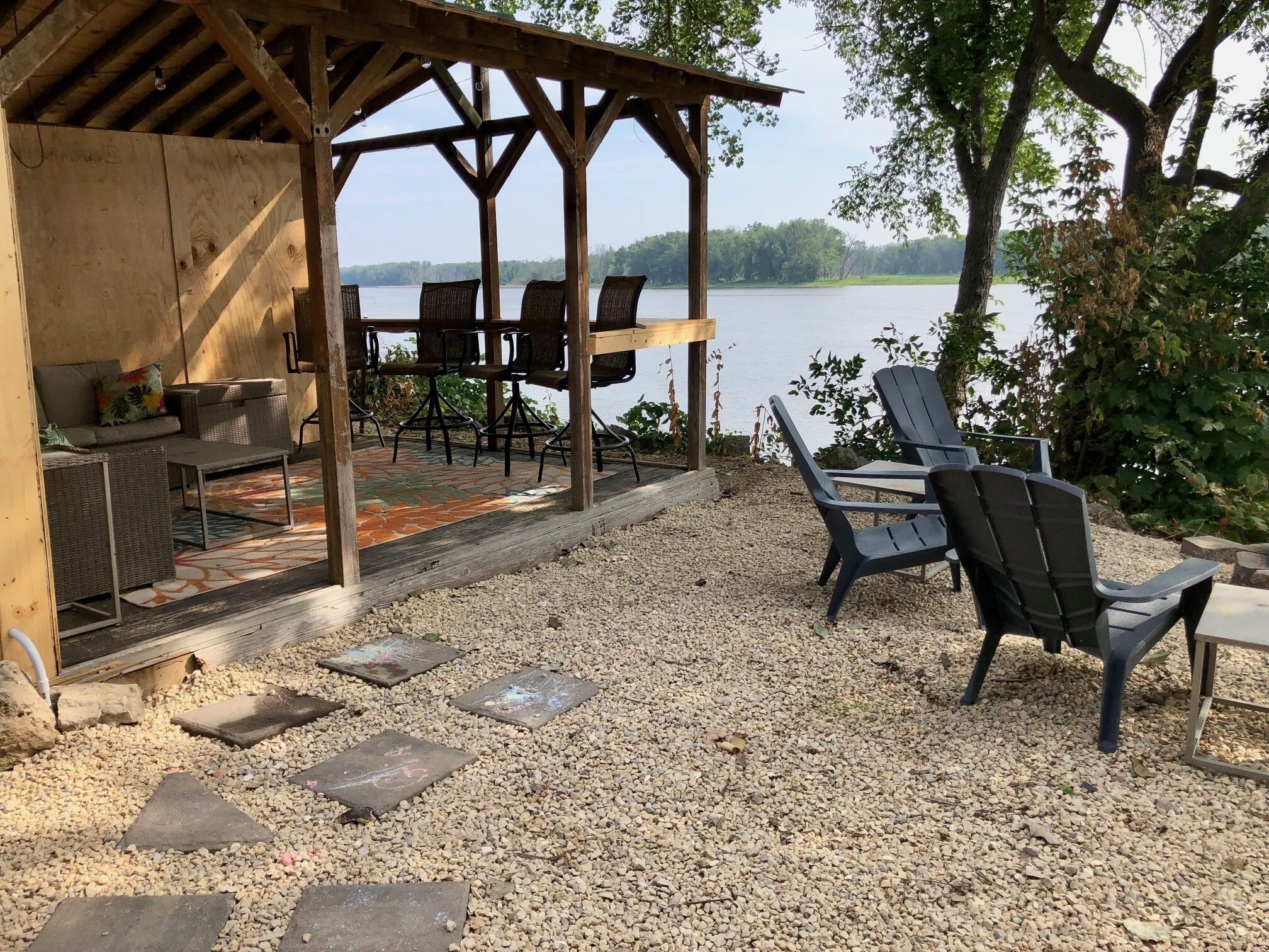 A covered outdoor seating area with chairs and tables, a wooden pergola, and a view of a lake.