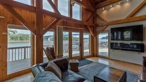 A spacious living room with a large wooden ceiling, a leather sofa, a coffee table, and a TV mounted on the wall. - Water Street Lodge! Waterfront 4 Bedroom, 4 Bath, Sleeps 12! (Marquette)