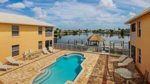 A swimming pool with lounge chairs and a table, surrounded by a building with a view of a lake. - Casa Laura Unit B - Lake Louise with a private pool (Cape Coral)